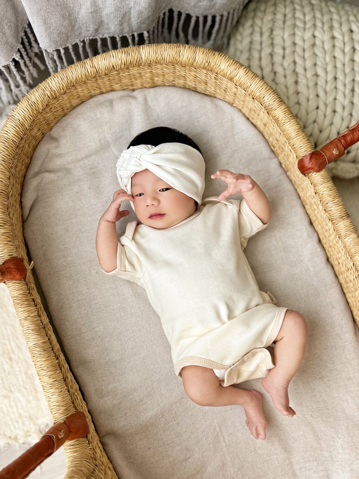 Baby in a organic cotton white onesies and headband lying in a blasket with neutral tones | Eotton Canada
