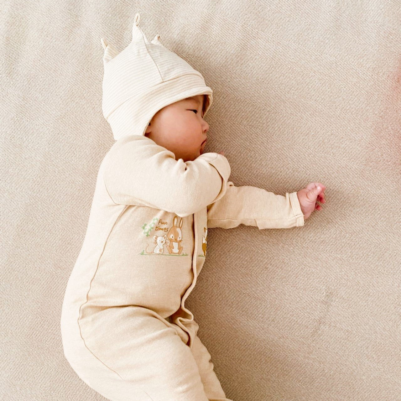 Sleeping baby wearing an unbleached nature colored cotton crown beanie in a soft classic stripe pattern layout.