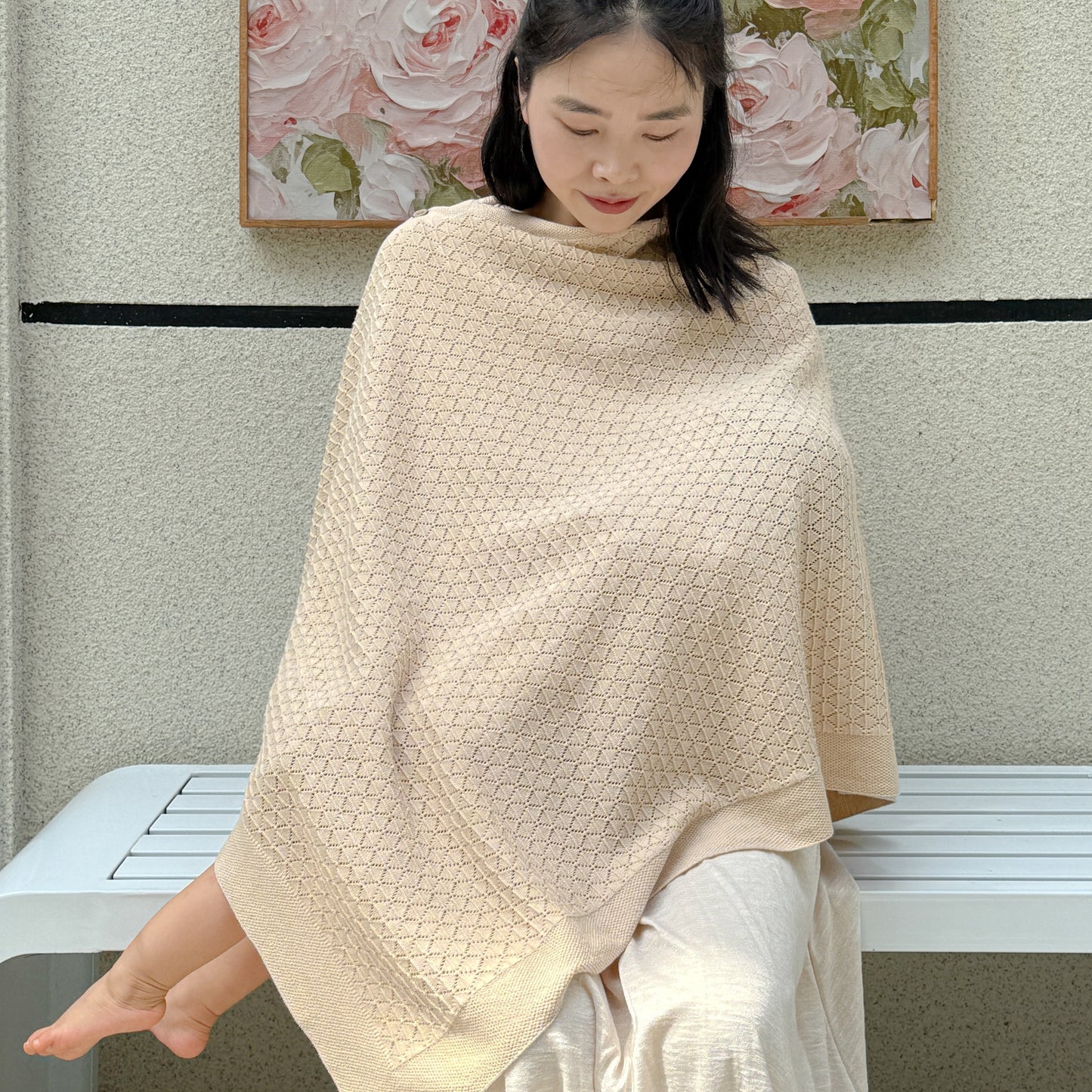 Model showing the lightweight 12G geometric pointelle knitwear texture of the multi-use organic infant sweater shawl and feeding cover