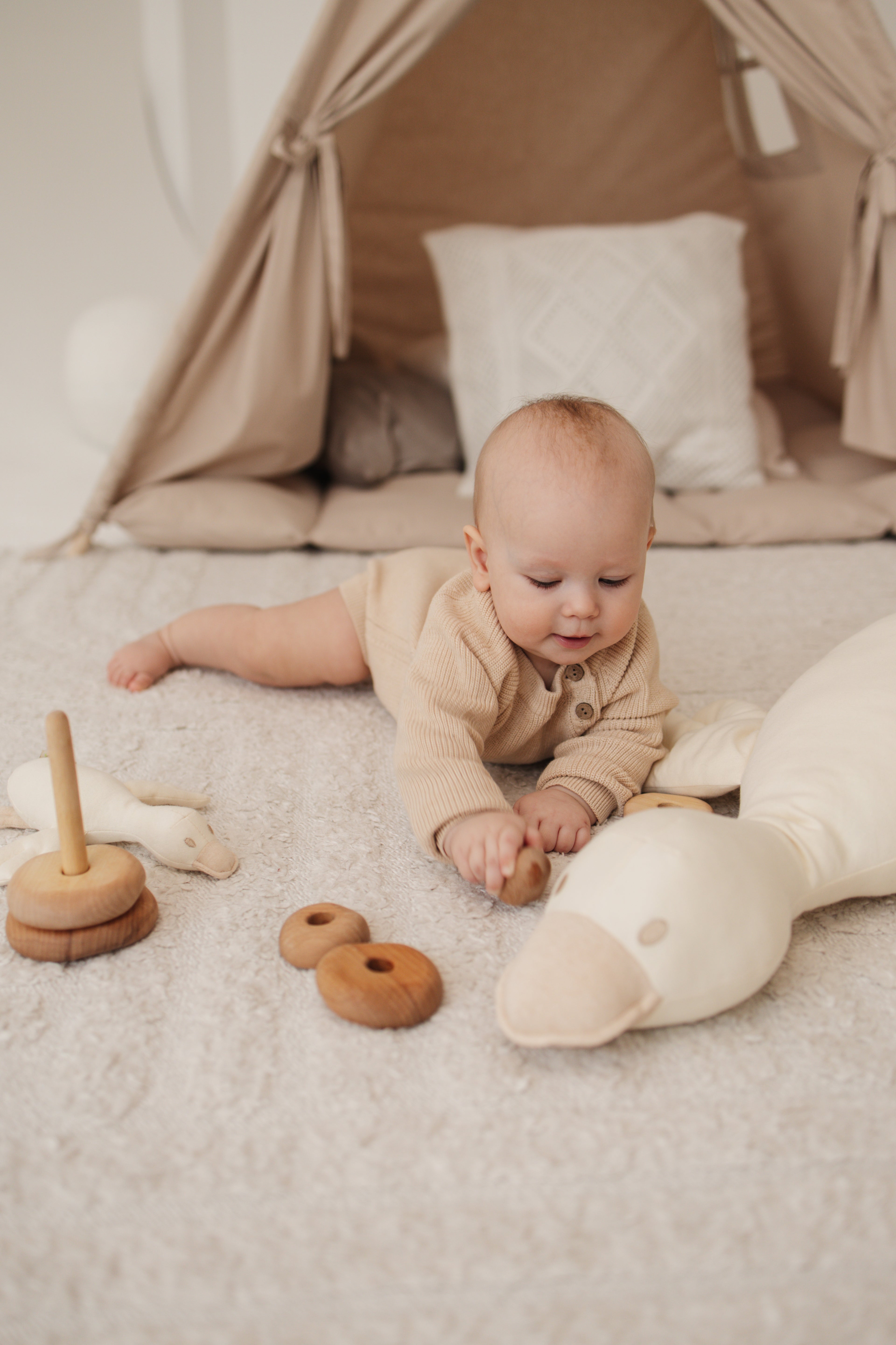baby dressed in organic nature colored cotton sweater playing with the cute organic baby toys on floor