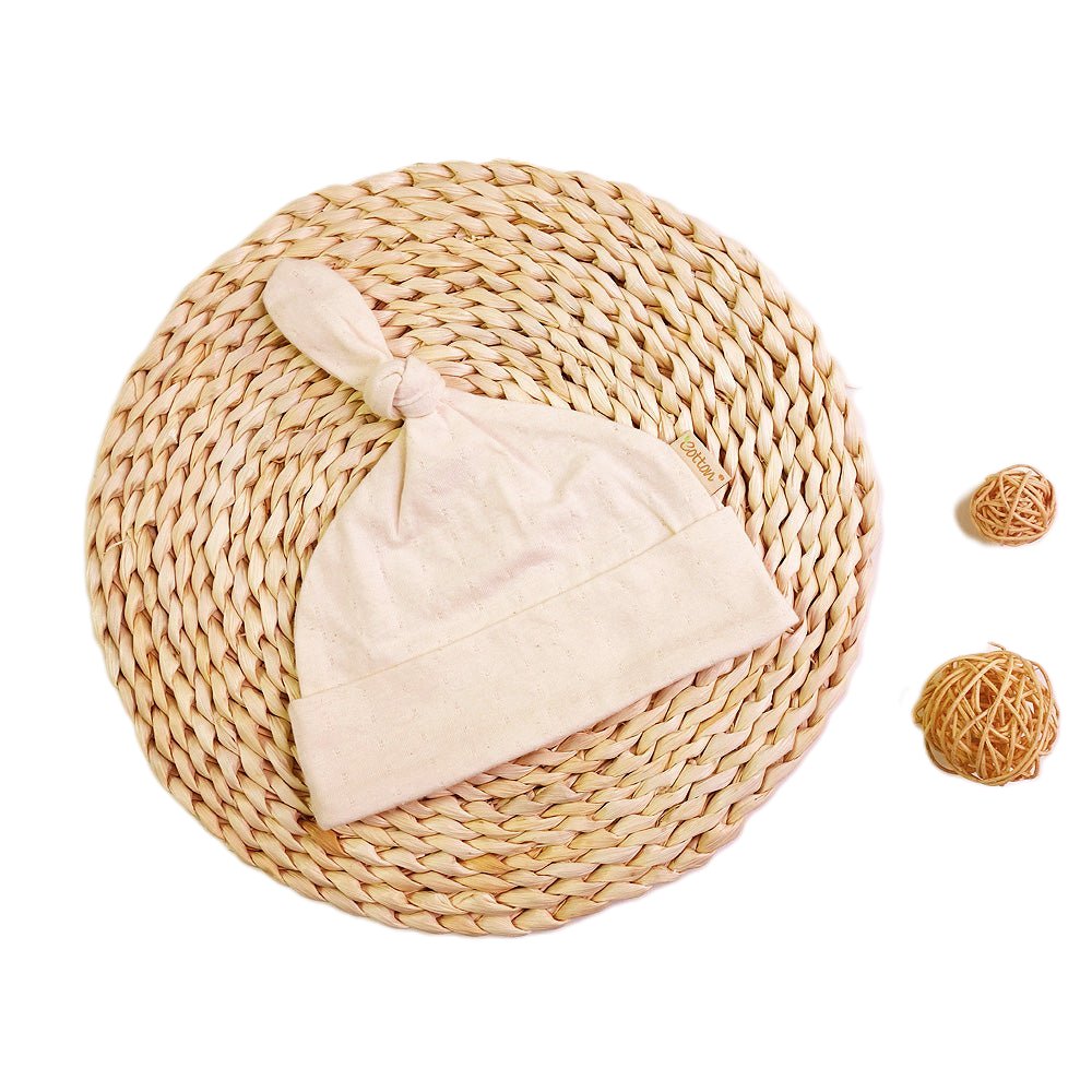 Organic baby summer hat made from breathable nature white jacquard single jersey cotton laid flat on a rustic woven mat.