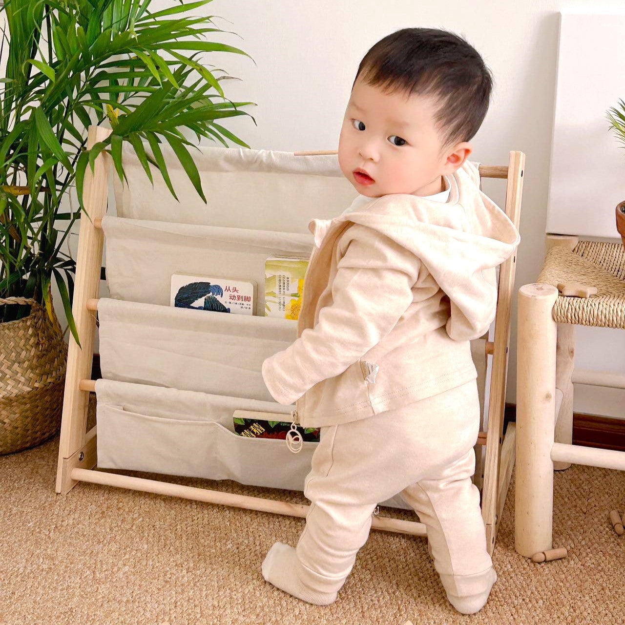An active baby boy playing in a natural cream two piece organic cotton tracksuit featuring a long sleeve top and matching comfy jogger pants