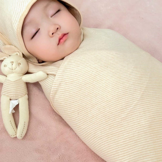 Organic newborn swaddle wrap enclosing a sleeping infant comfortably on a nursery mattress.