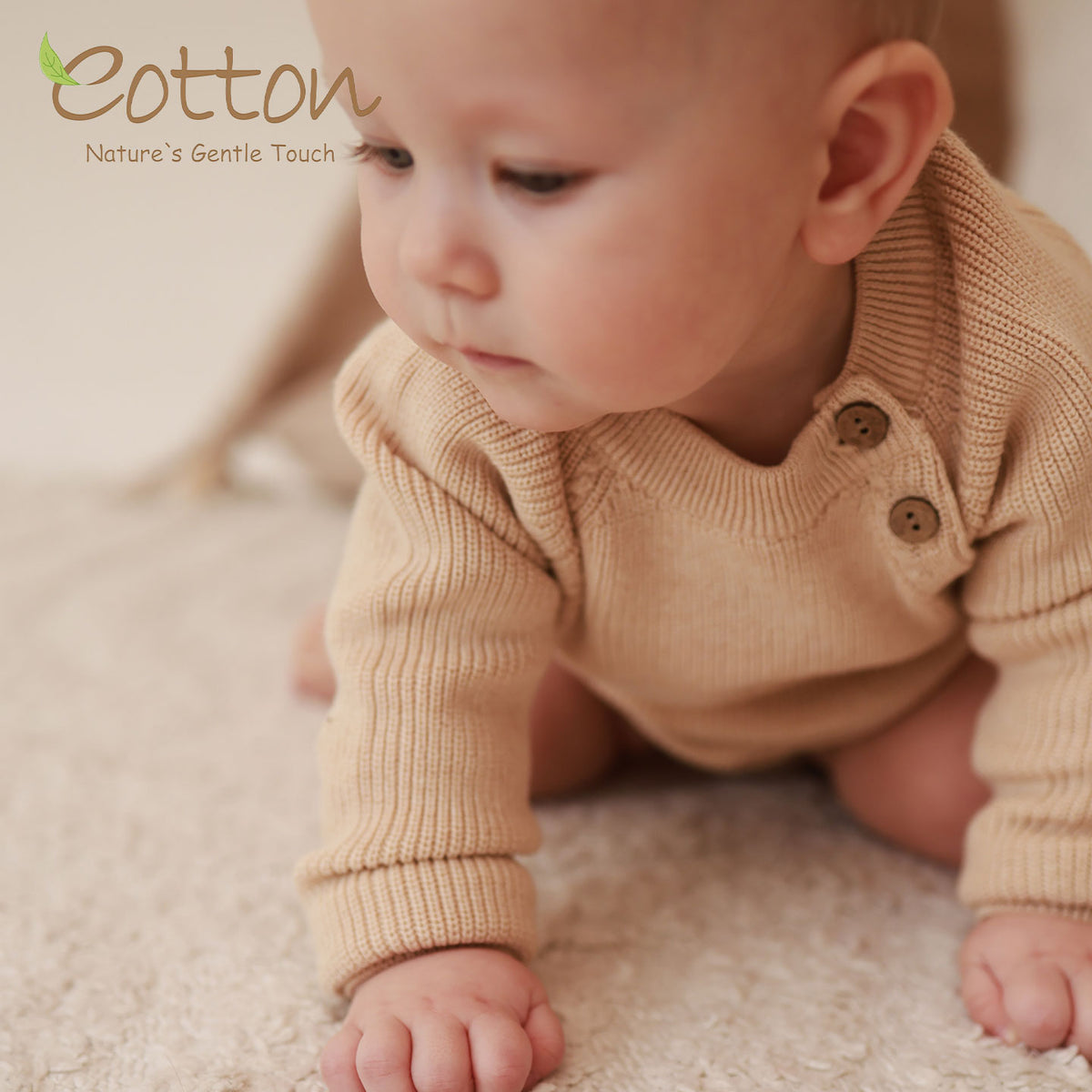 Close up of seated baby wearing a beige side button knitted baby sweater bodysuit