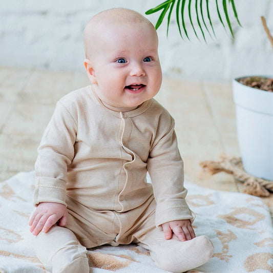 Happy footed organic cotton romper worn by a smiling baby sitting comfortably on a soft blanket.