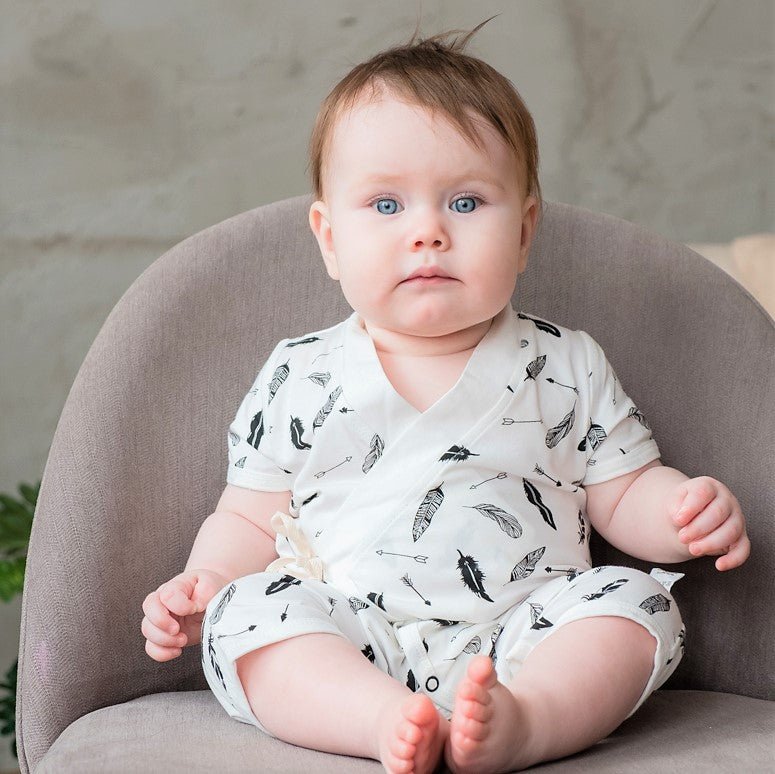 Active newborn baby lying comfortably on a soft surface wearing the monochrome feather pattern wrap romper.