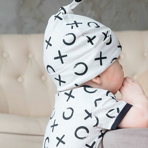 Close up view of a newborn baby sleeping peacefully while wearing the white organic cotton adjustable beanie with black XO print.